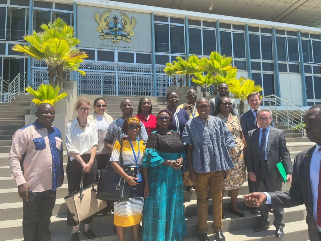 A group photo of Members of Parliament and UNPRPD officials standing in front of the Parliament House with a sign that reads "House of Parliament.